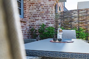 A table with a bottle of liquor, glasses, and a menu, set against a brick wall and wicker fence.