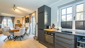 A modern kitchen with dark cabinetry, a built-in oven, and a large window with blinds. - Haus Rosi - Holiday home in Westerland with sauna and garden. Pets are (Sylt)
