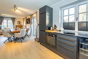 A modern kitchen with dark cabinetry, a built-in oven, and a large window with blinds. - Haus Rosi - Holiday home in Westerland with sauna and garden. Pets are (Sylt)