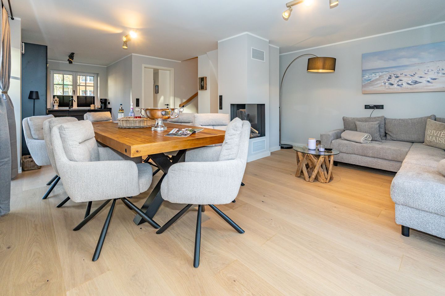 Un salon moderne avec une table à manger en bois, des chaises grises à revêtement, un canapé gris et une table basse ronde.