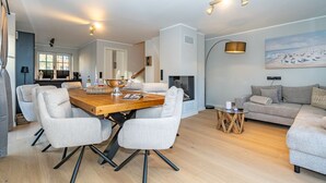 A modern living room with a wooden dining table, grey upholstered chairs, a grey sofa, and a round coffee table. - Haus Rosi - Holiday home in Westerland with sauna and garden. Pets are (Sylt)