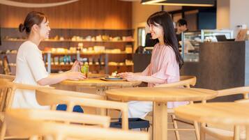 Two people seated at a wooden table in a cafe with a modern interior, including a counter and shelves with various items.