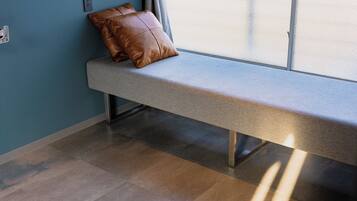 A bench with a brown cushion against a wall with a window.