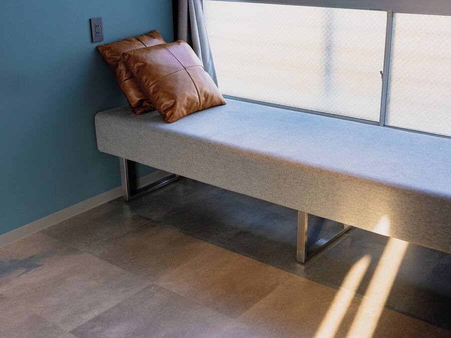 A bench with a brown cushion against a wall with a window.