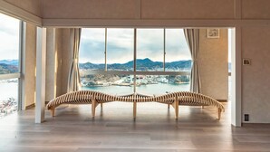 A spacious room with a large window offering a view of a river and mountains. There are two wooden benches in the center. - onomichi club (Onomichi)