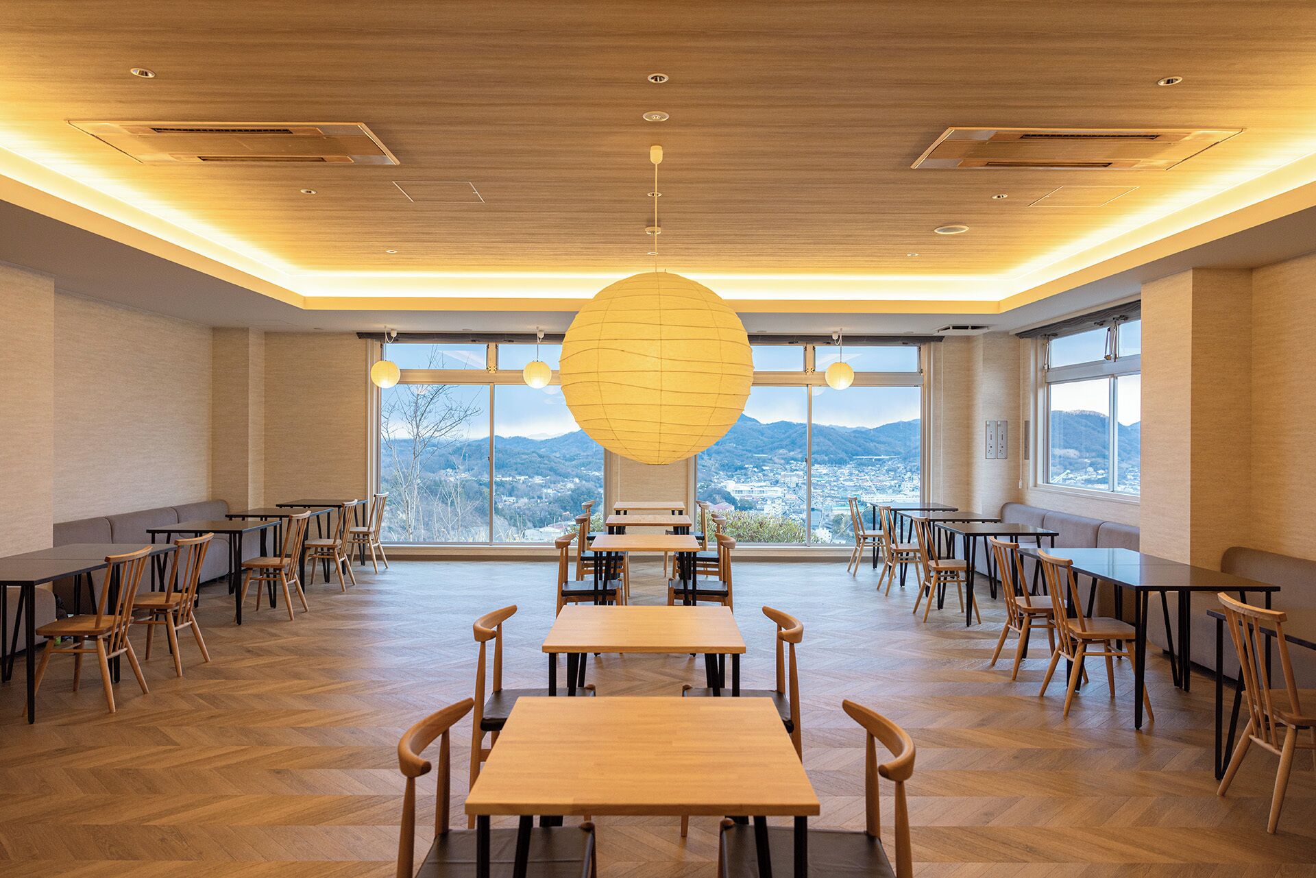 A spacious dining area with wooden tables and chairs, large windows offering a view of mountains, and a unique spherical light fixture.