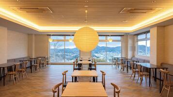 Un comedor espacioso con mesas y sillas de madera, ventanas amplias que ofrecen vistas a montañas, y una lámpara esférica distintiva.