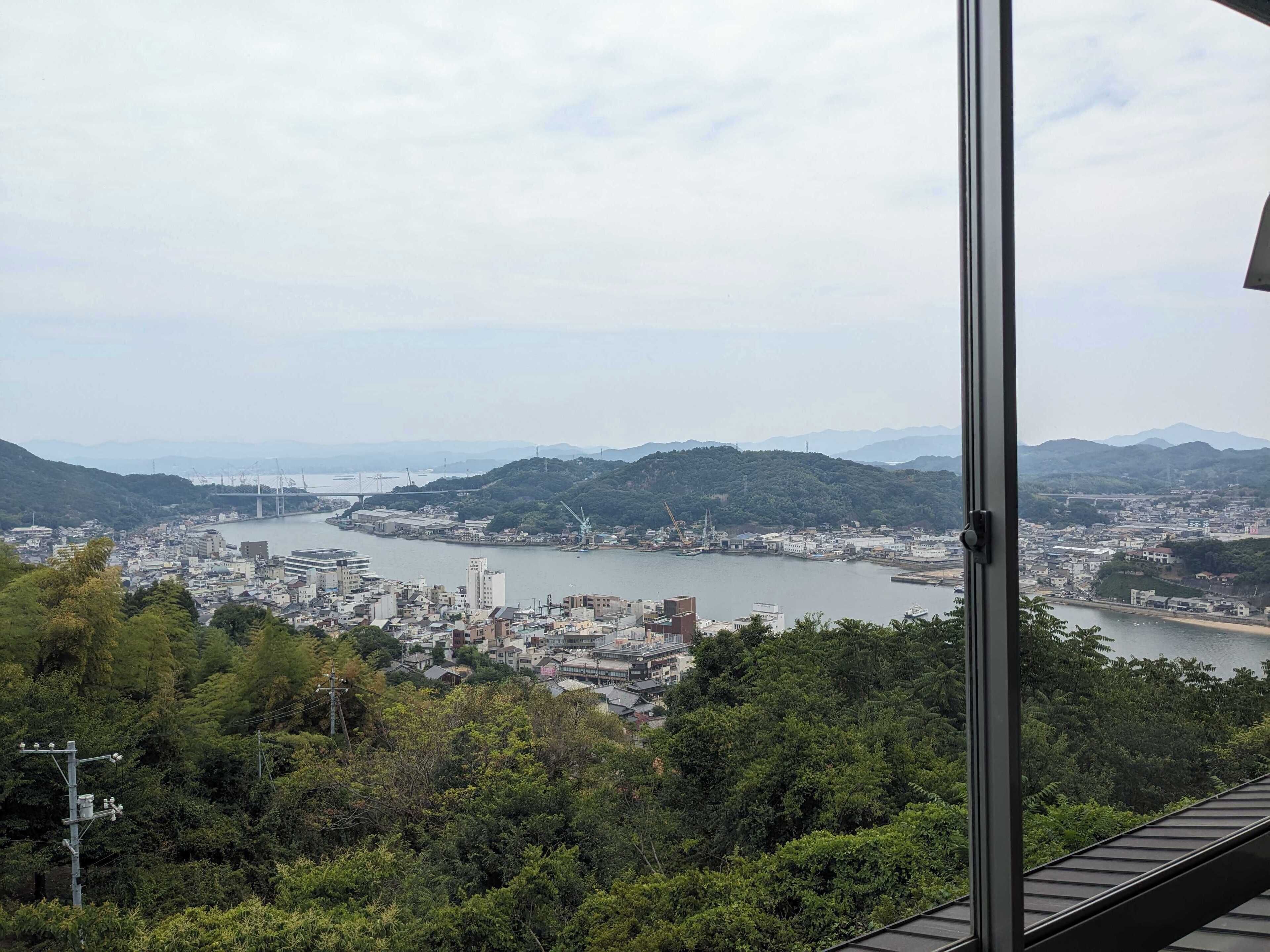 A panoramic view of a coastal city with a river, hills, and a bridge.