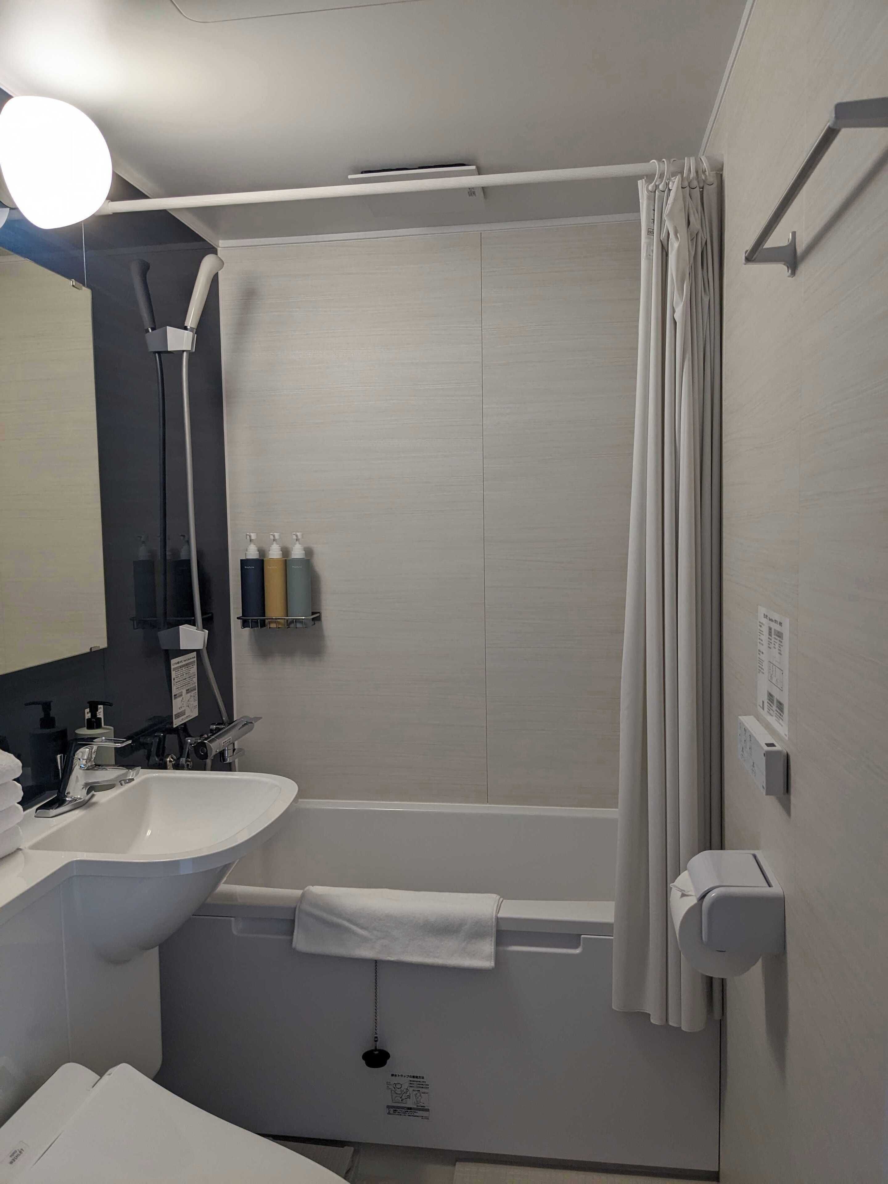 Een moderne badkamer met een bad, een wastafel en een spiegel. Er staan toiletartikelen op de muur en een handdoek hangt aan de badkuip.