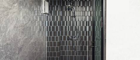 A modern shower with a vertical striped tile design, a handheld showerhead, and a glass door.