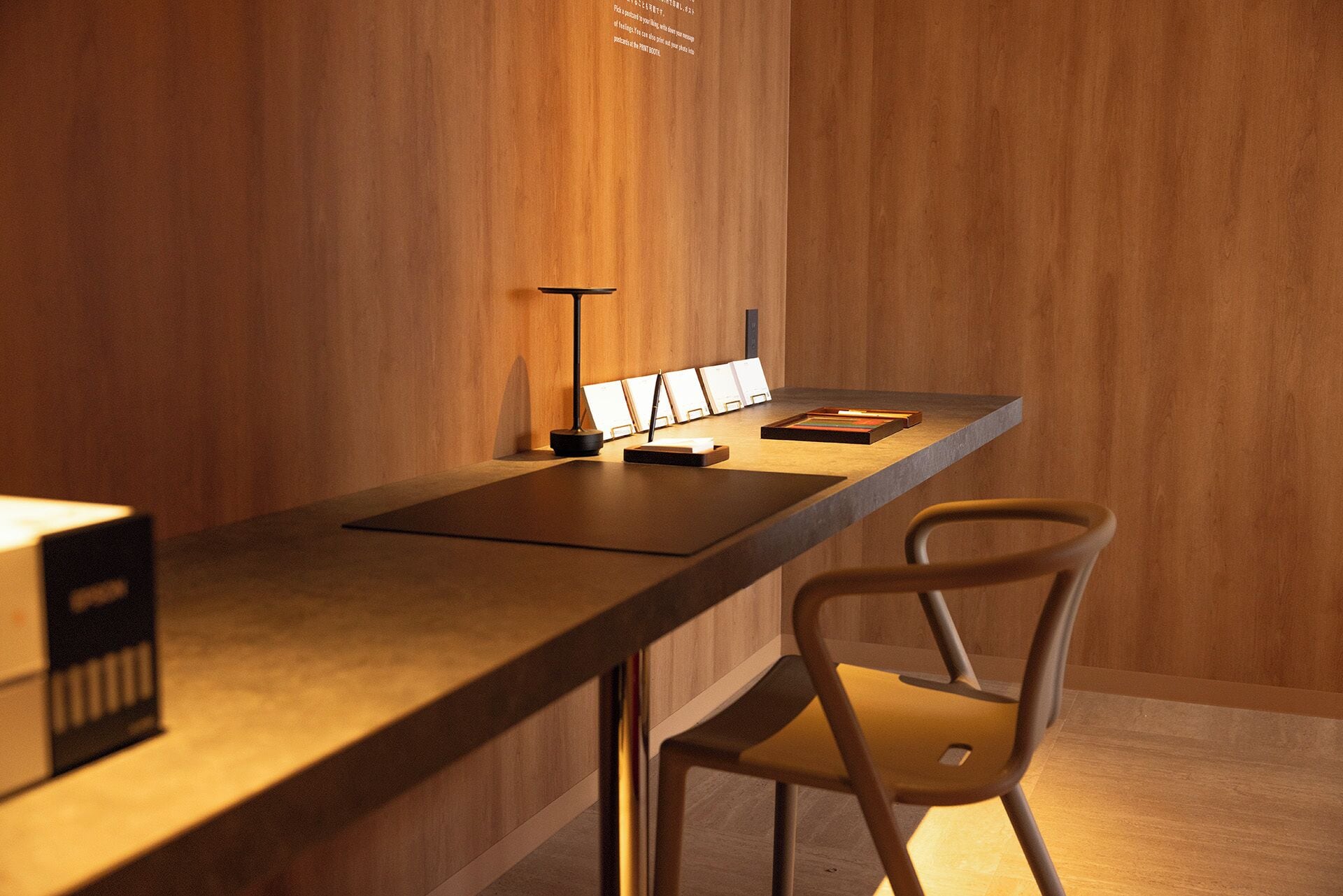 A modern workspace with a long desk, a chair, and a lamp.