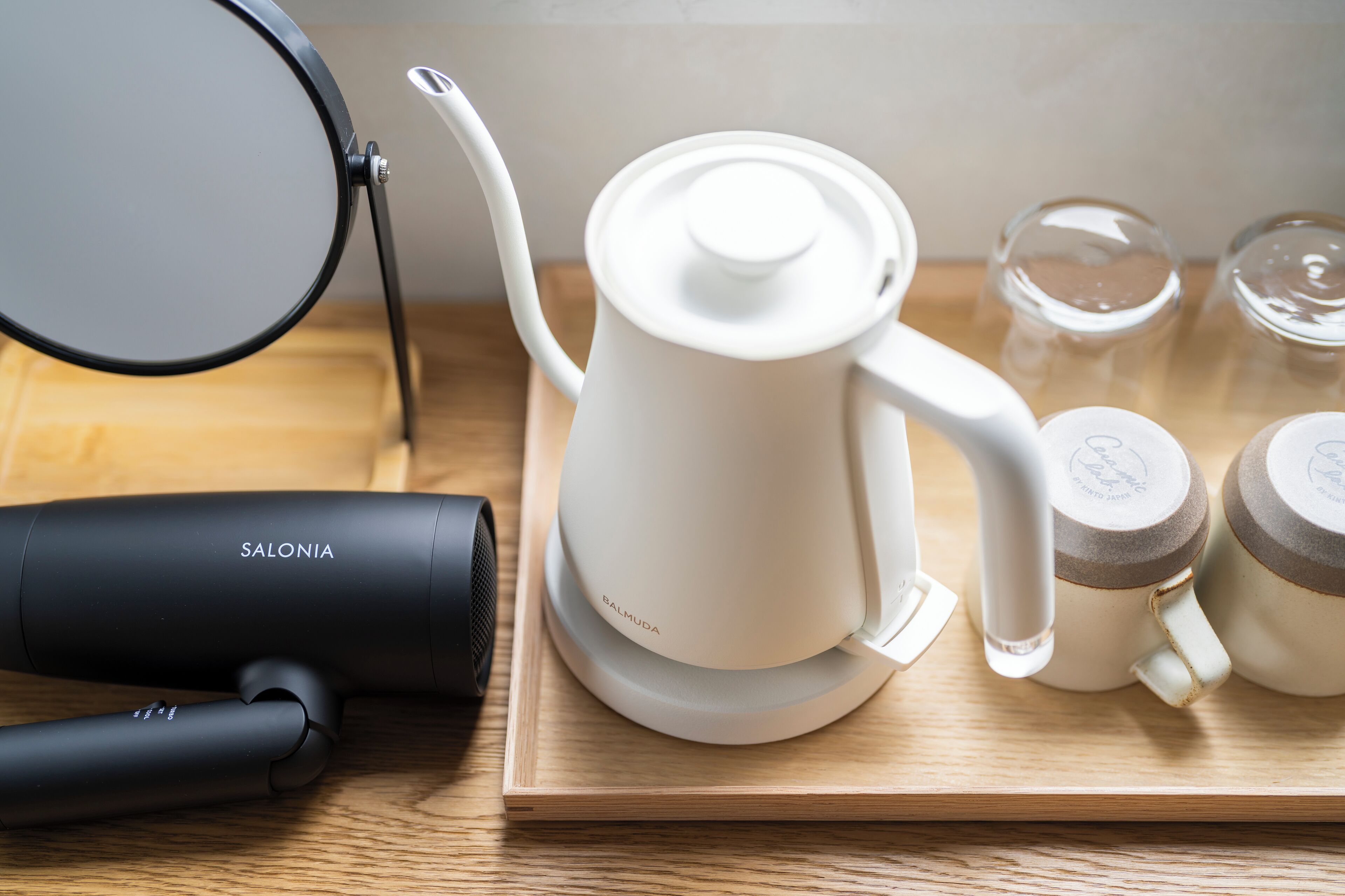 A coffee maker, a hair dryer, and two glass jars on a wooden tray.