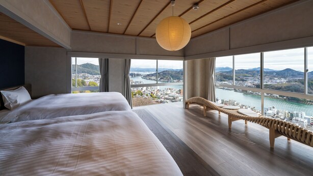A modern hotel room with two large beds, a wooden ceiling, and a view of a city and river. - onomichi club (Onomichi)