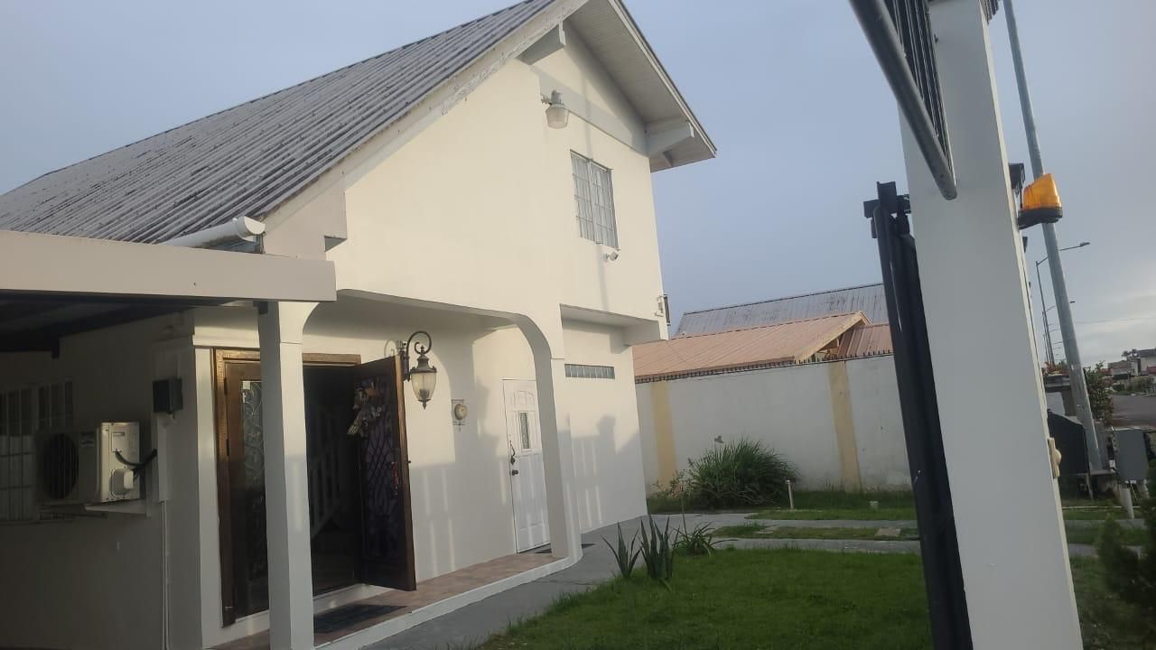 Una casa de dos pisos con un porche cubierto, un pequeño jardín y un equipo de aire acondicionado visible.