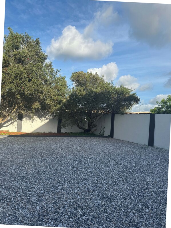 Une cour recouverte de gravier, avec des arbres et un mur blanc.