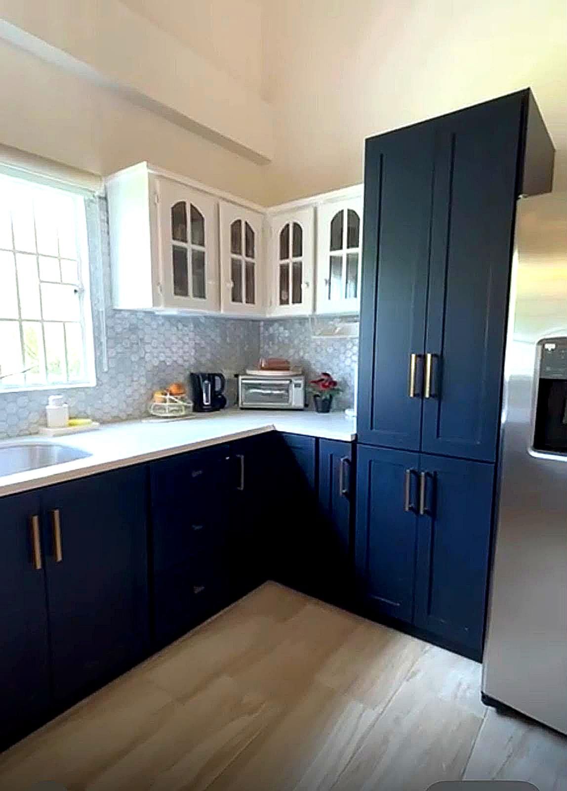 Una cocina con armarios azul oscuro, un refrigerador de acero inoxidable, un microondas y un ventanal con vistas.