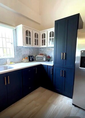Una cocina con armarios azul oscuro, un refrigerador de acero inoxidable, un microondas y un ventanal con vistas.