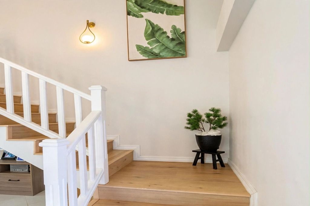 Una escalera con barandillas blancas, una lámpara de pared y una planta en maceta.