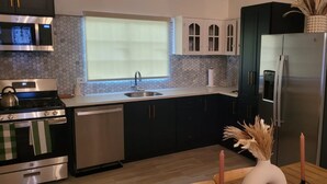 Una cocina moderna con electrodomésticos de acero inoxidable, una ventana con persianas y armarios oscuros.