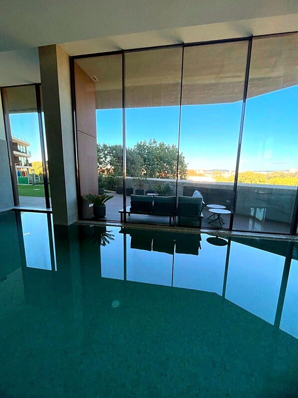 A room with a large window, a reflective floor, and a seating area with a view of the outdoors.