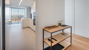 Eine moderne Küche mit weißen Schränken, einem Holztisch und Blick auf die Stadt durch große Fenster.