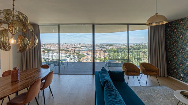 Ein modernes Wohnzimmer mit einer großen Schiebeglasdoor, die auf einen Balkon führt, einem Essbereich mit Holztisch und -stühlen sowie einem blauen Sofa.