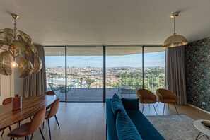 Una sala de estar moderna con un amplio ventanal corredero que da a un balcón, una zona de comedor con una mesa y sillas de madera, y un sofá azul.