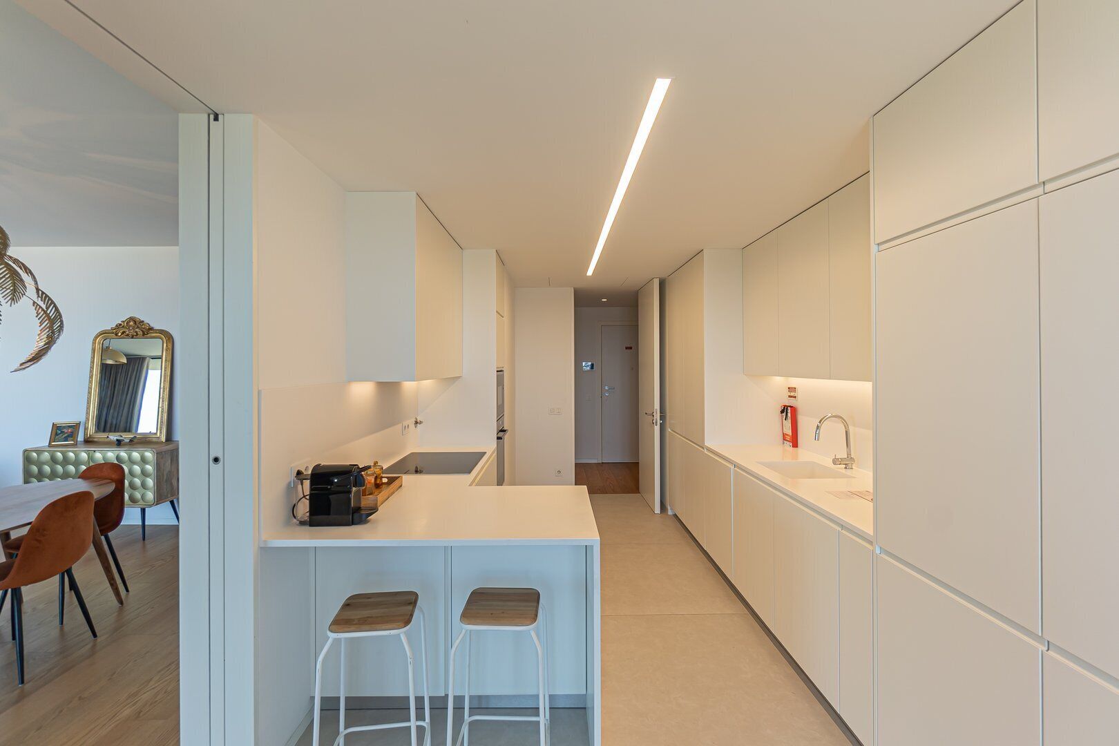 A modern kitchen with white cabinetry, a central island with stools, and a dining area with a vintage chair.