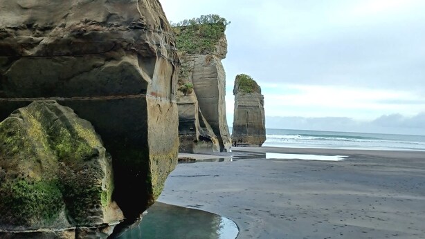 A coastal landscape with rock formations and a beach. - Kereru Creek by Tiny Away (Tataraimaka)