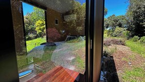 A modern house with large glass windows, a wooden deck, and a garden with various plants and a lawn. - Kereru Creek by Tiny Away (Tataraimaka)