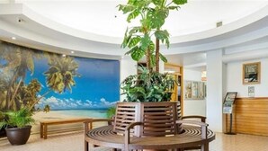 Eine Lobby mit einer zentralen Sitzecke, einem großen Wandgemälde einer Strandansicht und einem Empfangsbereich.