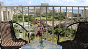 Ein Balkon mit Korbstühlen, einem Tisch und einer Blumenvase, mit Blick auf die Stadt.