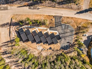 An aerial view of a parking area with multiple rows of solar panels, a paved walkway, and a small building structure.