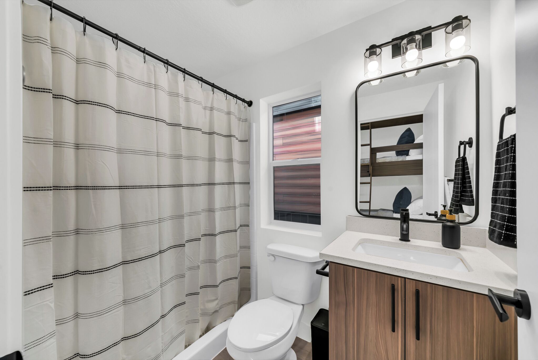 A modern bathroom with a shower curtain, toilet, sink, mirror, and vanity.