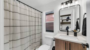 A modern bathroom with a shower curtain, toilet, sink, mirror, and vanity.