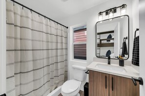 A modern bathroom with a shower curtain, toilet, sink, mirror, and vanity.