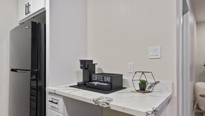 Eine kleine Küchenzeile mit einem Kühlschrank, einer Kaffeemaschine und einem Schild mit der Aufschrift 'Coffee Bar'.