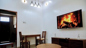 A living room with a TV displaying a fireplace, a dining table with chairs, and a sofa. - Ridge Estates - Bahari Beach (Dar es Salaam)