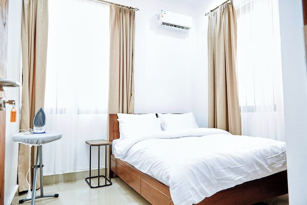 A neatly made bed with white linens, a small bedside table with an iron, and a wall-mounted air conditioner. - Ridge Estates - Bahari Beach (Dar es Salaam)