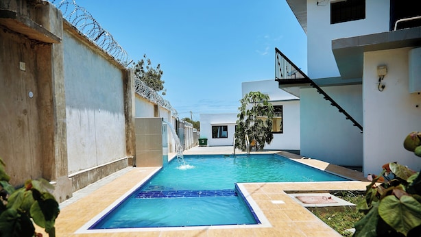 A swimming pool with a clear blue water, surrounded by a tiled deck and a concrete wall with barbed wire on top. - Ridge Estates - Bahari Beach (Dar es Salaam)