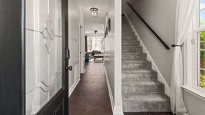 Un couloir doté d’un parquet en bois foncé, d’un escalier avec une main courante sombre et d’une porte ornée d’un motif géométrique en verre.