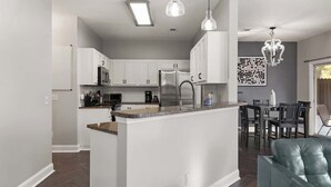 Une cuisine moderne avec des meubles blancs, un îlot central et un coin repas comprenant une table et des chaises.