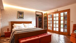 Een slaapkamer met een houten bed, een rode bank, een boekenkast en een deur met ruitpanelen.