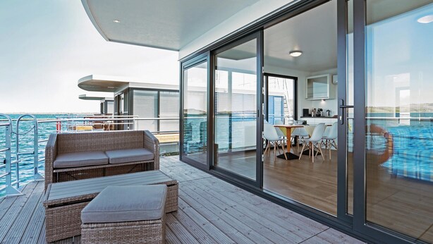 Eine moderne Terrasse mit Korbmöbeln, einem Essbereich und Blick auf das Meer.
