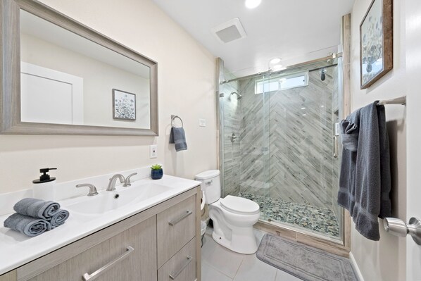 A modern bathroom with a large mirror, two sinks, a toilet, and a glass-enclosed shower.