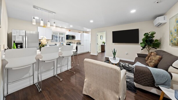 Una sala de estar moderna con un sofá, una mesa de centro y una zona de comedor con taburetes de bar.