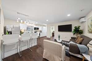 A modern living room with a sofa, a coffee table, and a dining area with bar stools.