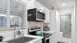 Una cocina moderna con armarios blancos, un microondas negro, un fregadero de acero inoxidable y una estufa.