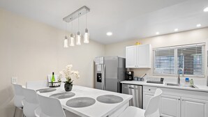 Una cocina moderna con armarios blancos, electrodomésticos de acero inoxidable y una zona de comedor con sillas y mesa blancos.
