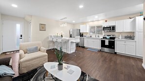 Una sala de estar moderna con un sofá, una mesa de comedor con sillas y una cocina con armarios y electrodomésticos blancos.